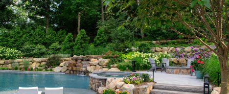 Custom Pool Spa and Tanning ledge with a raised firepit seating area and surrounding gardens.